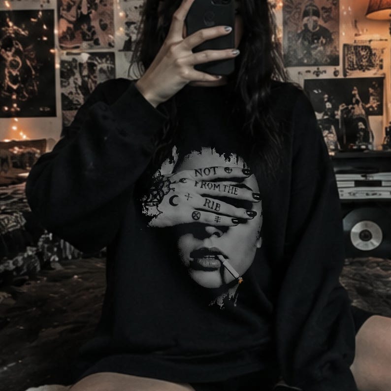 Alternative woman taking a mirror selfie in a black Lilith graphic sweatshirt, featuring the feminist “Not From the Rib” design in distressed grayscale.