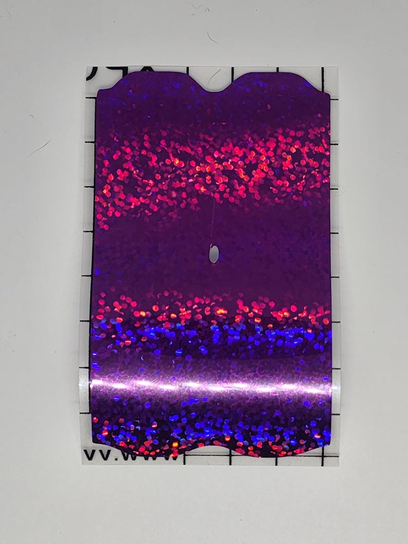 K&ouml;nnte beinhalten: Ein rechteckiger, schillernder Aufkleber mit einem lila, roten und blauen Glitzereffekt. Der Aufkleber hat eine abgerundete Oberkante und ein kleines Loch in der N&auml;he der Mitte. Der Aufkleber befindet sich auf einer transparenten R&uuml;ckseite mit schwarzen Rasterlinien.