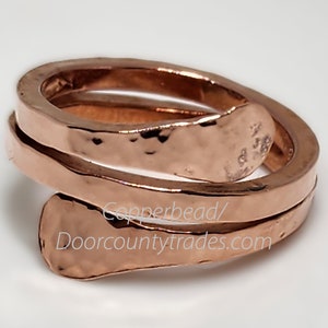 May include: A copper ring with a hammered finish. The ring is made of two bands that are twisted together. The ring is inscribed with "Copperbead/Doorcountytrades.com".