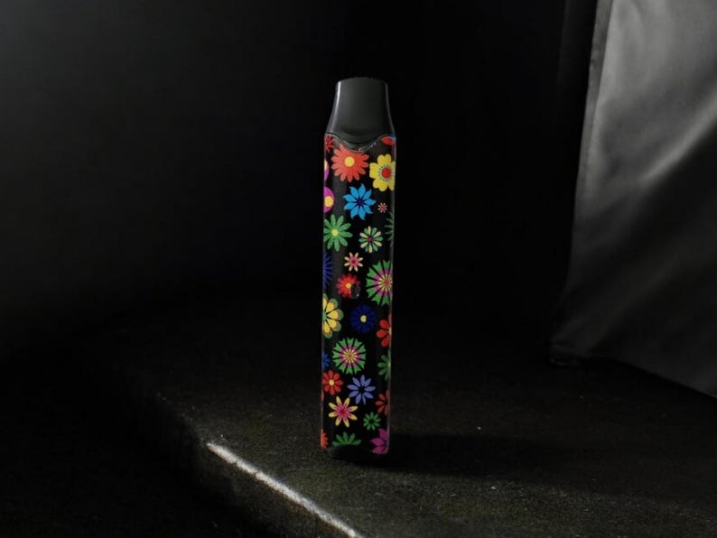 May include: A black vape pen with a colorful floral pattern. The flowers are in shades of red, yellow, blue, green, and purple.