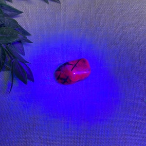K&ouml;nnte beinhalten: Ein rosa und schwarzer Kristall mit einer glatten, polierten Oberfl&auml;che. Der Kristall wird von einem blauen Licht beleuchtet, das seine komplizierten Muster hervorhebt.