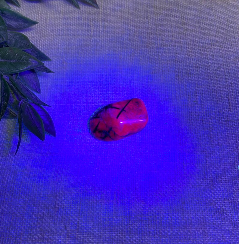 K&ouml;nnte beinhalten: Ein rosa und schwarzer Kristall mit einer glatten, polierten Oberfl&auml;che. Der Kristall wird von einem blauen Licht beleuchtet, das seine komplizierten Muster hervorhebt.