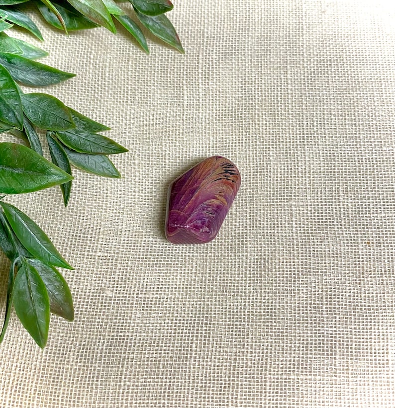 May include: A purple and brown gemstone with a unique swirling pattern. The stone is smooth and polished, and it has a natural, organic shape.