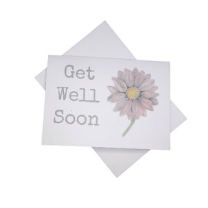 May include: A white card with the text "Get Well Soon" in gray lettering and a pink flower with a yellow center.