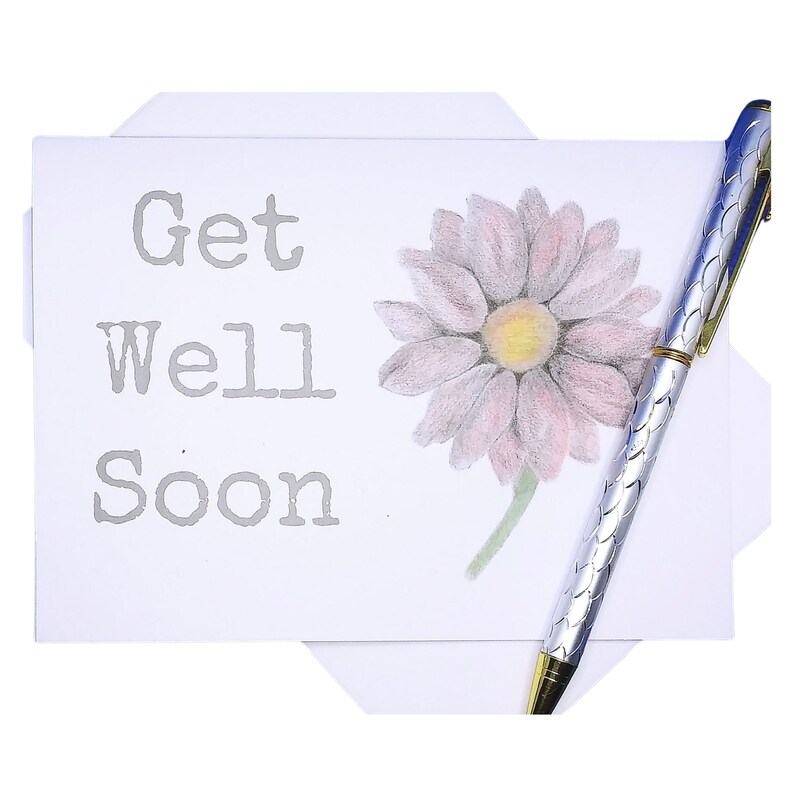 May include: A white card with the text "Get Well Soon" in gray lettering. A pink flower with a yellow center is drawn on the card. A silver pen with a gold tip is lying on the card.