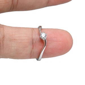 May include: A silver ring with a single, clear, round gemstone set in a prong setting. The ring has a curved band.