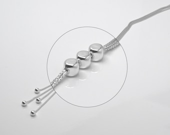 Peut inclure: Un collier en argent avec une chaîne et quatre perles rondes. Le collier a un pompon avec cinq petites perles à l'extrémité.