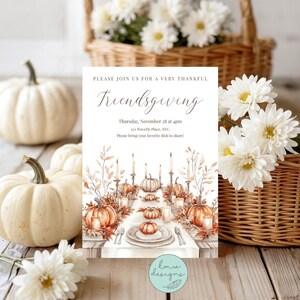 May include: Thanksgiving-themed invitation with the text "Friendsgiving." The invitation features a watercolor illustration of a festive table setting with pumpkins, candles, and fall foliage. White pumpkins and flowers in a basket are in the background.