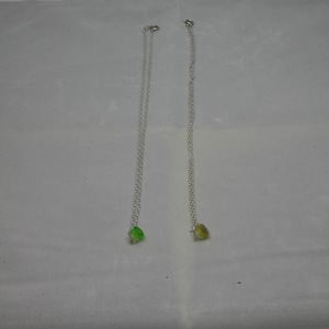 Op de afbeelding: Twee zilveren kettingen met kleine bedels. Een bedel is groen en de andere is geel.