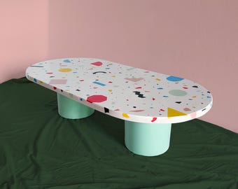 Pode incluir: Mesa de centro oval com tampo branco com um padrão geométrico colorido. A mesa tem duas pernas cilíndricas verde claro.