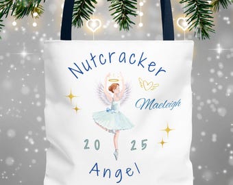 May include: White tote bag with navy blue handles featuring a ballerina angel design. The design includes the words "Nutcracker Angel" and the name "Maeleigh" in blue script, along with the year "2025" and star accents.