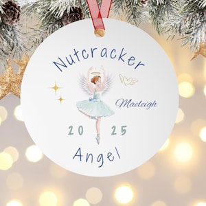 Könnte beinhalten: Ein weißer Weihnachtsschmuck mit rotem Band. Der Schmuck zeigt eine Aquarellillustration eines Ballerina-Engels mit den Worten "Nutcracker", "Maeligh", "20 25" und "Angel" in blauer Schrift.