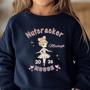 May include: Dark blue sweatshirt with a ballerina mouse graphic and the words "Nutcracker" and "Mouse". The design includes the name "Maeleigh", the numbers "20" and "26", and pink hearts and stars.