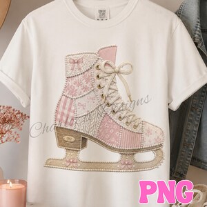 May include: A white short-sleeve t-shirt featuring a large graphic of an ice skate. The skate is decorated with a patchwork pattern of pink and white floral, plaid, and knit textures, accented with small bows and a border of white pearls.