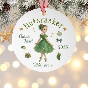 Può includere: Ornamento natalizio rotondo con un'illustrazione ad acquerello di una ballerina in un vestito verde. L'ornamento presenta il testo "Nutcracker", "Clara's Friend", "2025" e il nome "Marissa". Elementi decorativi: stelle, un fiocco e un regalo.