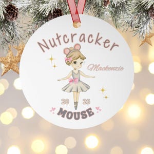 May include: White round Christmas ornament with a ballerina mouse illustration. The ornament has the text "Nutcracker" and "Mackenzie" in pink. The ballerina mouse is wearing a gray dress and a pink bow. The text "20 25 Mouse" is also on the ornament.