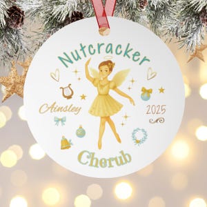 May include: A white Christmas ornament with a red ribbon. The ornament features a watercolor illustration of a cherub ballerina with the text "Nutcracker", "Ainsley", "Cherub", and the year "2025". Decorative elements include hearts, stars, and bows.
