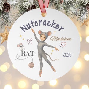 May include: A white Christmas ornament with a red ribbon. The ornament features a watercolor illustration of a child in a gray mouse costume, with the text "Nutcracker", "Madeline", "Rat", and "2025".