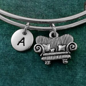 May include: A silver charm bracelet with a personalized letter 'A' charm and a charm shaped like a couch. The bracelet is on a green background.