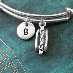 May include: A silver charm bracelet with a hot dog charm and a charm with the letter B.