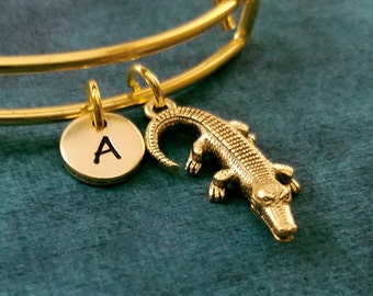 Puede incluir: Un brazalete expandible de oro con un dije de cocodrilo de oro y un dije de oro con la letra A.