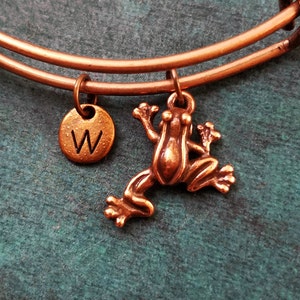 May include: A copper-toned expandable bracelet with a frog charm and a small round charm with the letter 'W' engraved on it.