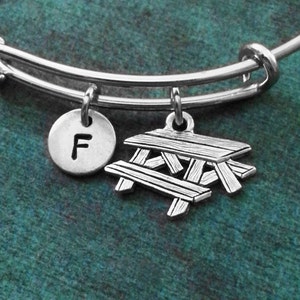 May include: A silver charm bracelet with a silver charm of a picnic table and a silver charm with the letter F.