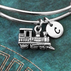 May include: A silver expandable bracelet with a charm of a silver toy train and a silver charm with the letter "C" on it.