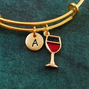 May include: Gold charm bracelet with a red wine glass charm and a letter A charm.