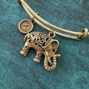 May include: A gold charm bracelet with an elephant charm and a letter 'A' charm. The elephant charm has intricate details and is facing to the right.