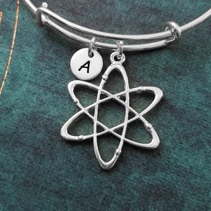 May include: A silver charm bracelet with a silver atom charm and a silver charm with the letter A.