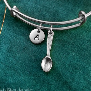 Könnte beinhalten: Ein silbernes Armband mit einem Löffel-Anhänger und einem Anhänger mit dem Buchstaben A.