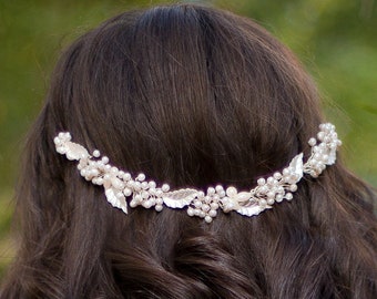 May include: A woman with long, dark brown hair wearing a white lace dress with a pearl and silver floral hairpiece.