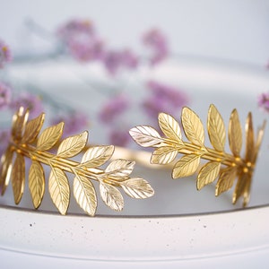 May include: A gold leaf headband with a delicate design. The headband is made of metal and features a series of leaves that are connected together. The headband is perfect for adding a touch of elegance to any outfit.