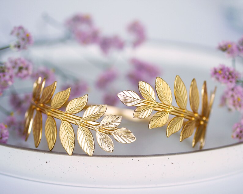 May include: A gold leaf headband with a delicate design. The headband is made of metal and features a series of leaves that are connected together. The headband is perfect for adding a touch of elegance to any outfit.