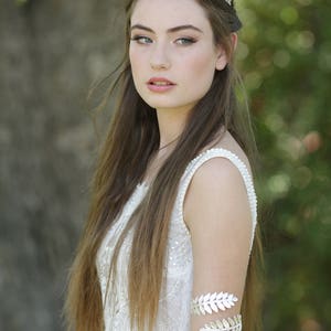 May include: A woman wearing a white lace dress with a silver leaf headband and matching silver leaf arm cuff.