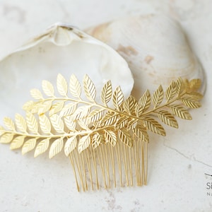 May include: Gold leaf hair comb with a delicate branch design. The comb is made of metal and has a gold finish. It is a beautiful and elegant hair accessory.