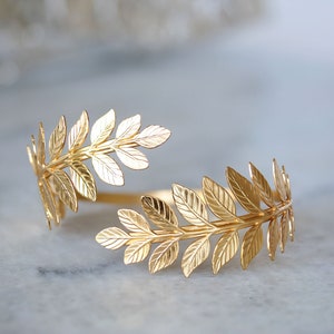 May include: A gold-toned leaf-shaped bracelet. The bracelet is made of metal and has a delicate, feminine design.