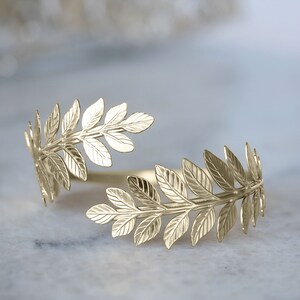 May include: Gold leaf branch ring with a delicate design. The ring is open and adjustable to fit most finger sizes.