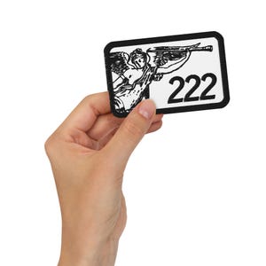 May include: A rectangular patch with a black border and a white background. The patch features a black illustration of an angel playing a trumpet, with the number "222" in bold black font.