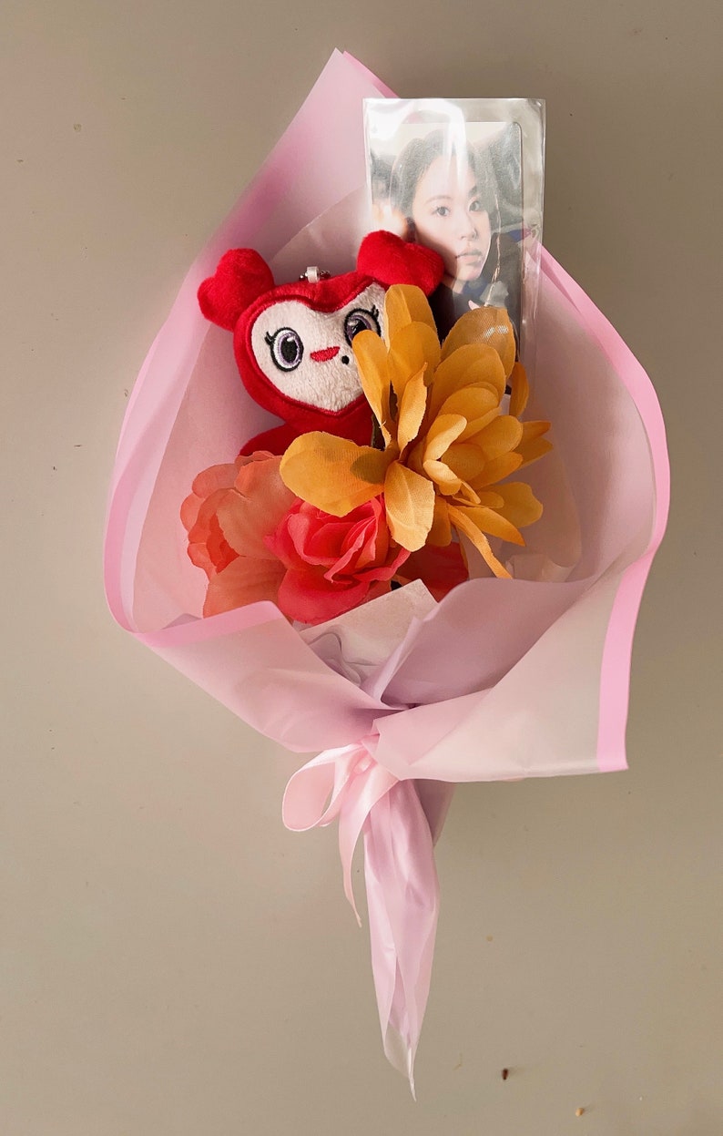 Puede incluir: Un ramo rosa con un juguete de peluche rojo, flores amarillas y rojas y una foto de una persona dentro de una funda de pl&aacute;stico transparente.