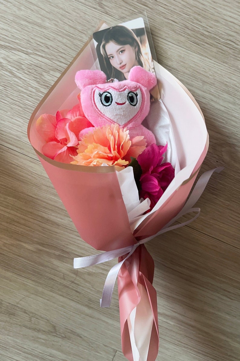 Puede incluir: Un ramo rosa con un juguete de peluche rosa con un coraz&oacute;n en el pecho y una tarjeta de foto en el interior. El ramo est&aacute; envuelto en papel rosa y atado con una cinta blanca.