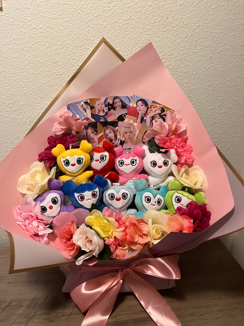 Puede incluir: Un ramo de flores rosas con peluches coloridos en forma de personajes de dibujos animados. El ramo est&aacute; envuelto en papel rosa con ribete dorado y atado con una cinta rosa.