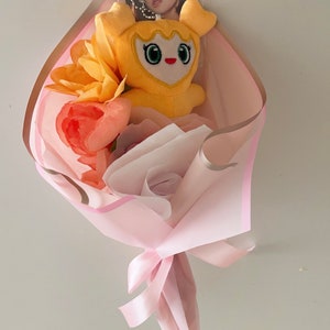 Puede incluir: Un ramo de flores artificiales rosa y marr&oacute;n con un juguete de peluche amarillo y una tarjeta de foto.