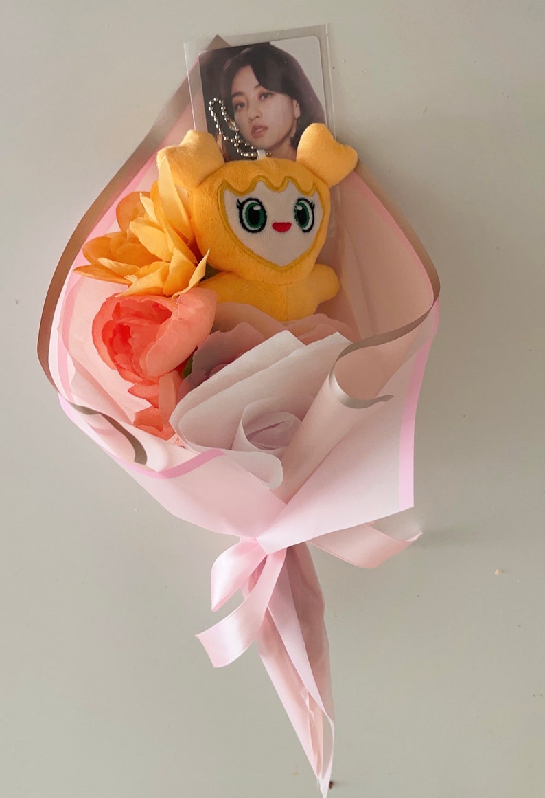 Puede incluir: Un ramo de flores artificiales rosa y marr&oacute;n con un juguete de peluche amarillo y una tarjeta de foto.