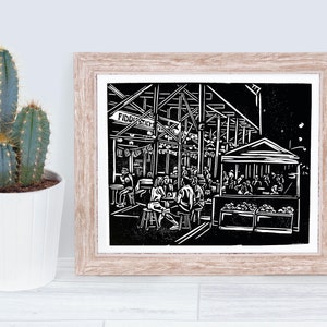 May include: Black and white linocut print of a bustling market scene. The print features a building with the text "Fiddlesticks" above the entrance. People are sitting at tables and enjoying food and drinks.