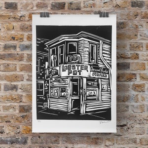 May include: Black and white linocut print of a shop front with the words "Lobster Pot" and "Charcoal Broiled Steaks" above the entrance. The print is signed "Doc" and numbered 95.