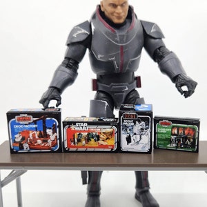 May include: Four vintage Star Wars action figure boxes on a brown folding table. The boxes are from the original Kenner line and feature the characters Darth Vader, Chewbacca, Luke Skywalker, and a Stormtrooper. The boxes are in good condition and have some wear and tear.