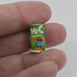 May include: Miniature Hi-C Ecto Cooler can. The can is green with the Hi-C logo in white and green. The text "Ecto Cooler" is below the logo. The can is held between two fingers.