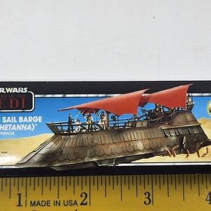May include: A Star Wars Return of the Jedi box for Jabba's Sail Barge (The Khetanna) vehicle. The box features a colourful image of the sail barge with red sails and a desert background. The text "Kenner" is visible in the bottom right corner.
